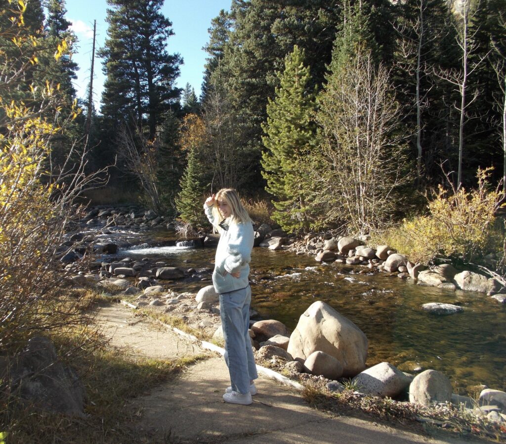 A girl is looking back at the camera in front of a river with trees backing the landscape